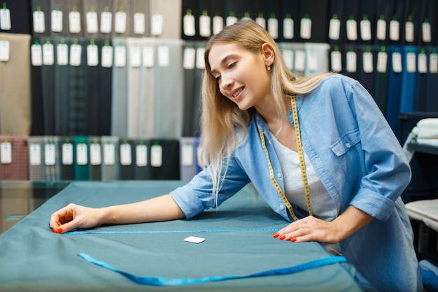 裁縫師は、テキスタイル ワークショップで生地の素材を測定します。裁縫用の布を扱う女性、職場の女性仕立て屋、洋裁職人