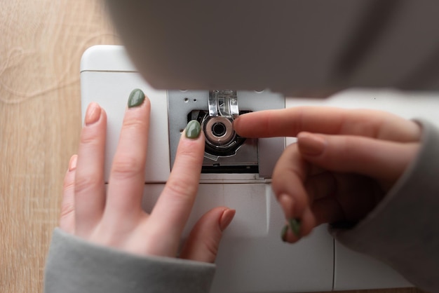 The seamstress replaces the bobbin in the sewing machine closeup of female hands with manicure small business concept