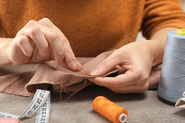 Seamstress sewing button on fabric at table in workshop