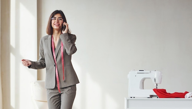 Seamstress talks by phone Young woman in formal clothes is indoors Conception of style