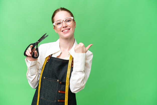 Seamstress woman over isolated chroma key background pointing to the side to present a product