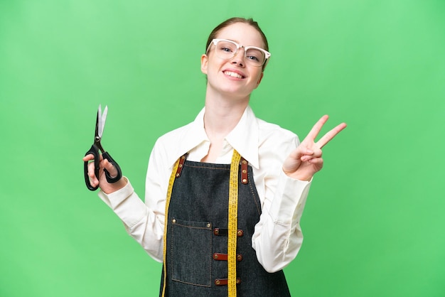 Seamstress woman over isolated chroma key background smiling and showing victory sign