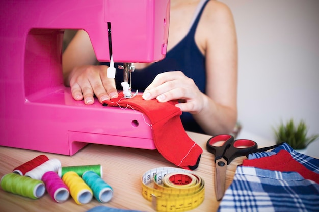 Seamstress working with sewing machine making trendy face medical mask for preventing and stop coronavirus spreading Homemade manufacturing concept Reuse of used clothes Main focus on fingers