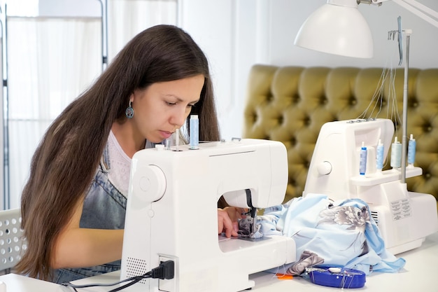 Seamstress works sewing on sewing machine in tailoring workshop business.