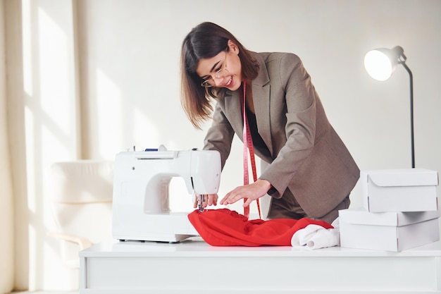 Seamstress works with red cloth Young woman in formal clothes is indoors Conception of style