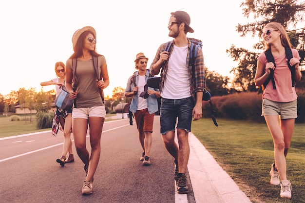 Photo in search of adventures. group of young people with backpacks walking together by the road and looking happy