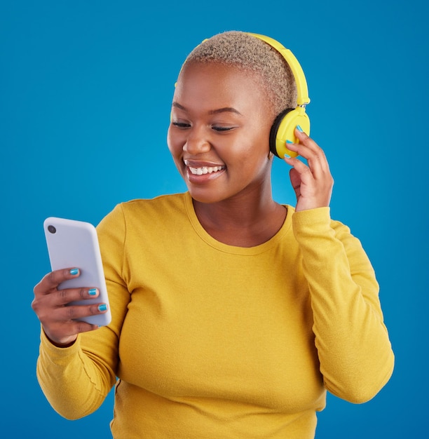 Search phone and music with black woman in studio for streaming multimedia and browsing Gen z smile and audio with female and headphones on blue background for listening online radio and songs