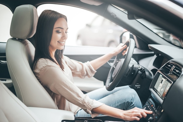 お気に入りの音楽を探しています。車を運転しながら笑顔でボタンを押す若い魅力的な女性