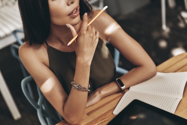 Searching for inspiration. Close-up of attractive young woman keeping hand on chin and mouth open while sitting in restaurant outdoors