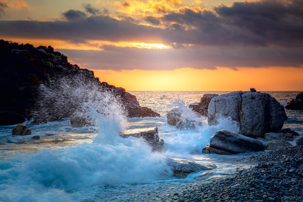 写真 海の風景 海の波がビーチの岩にぶつかり 海の水が太陽とともに空に飛び上がり 夕暮れ 海の嵐の風景 前景に焦点を当てる