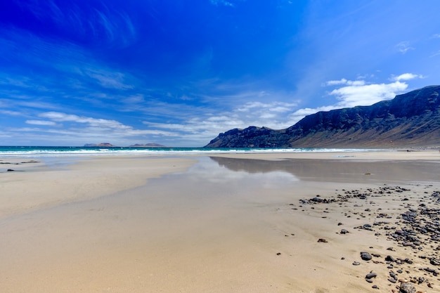 Photo seascape showing a large beach with water reflecting the blue sky