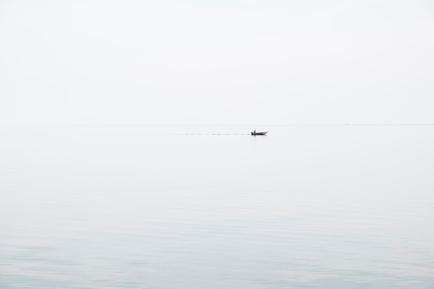 Seascape in the style of minimalism small fishing boat is\
minimal far in the blue sea between sky and water