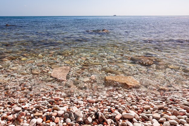 Фото Морской пейзаж с галечным берегом, чистой морской водой и кораблем в море