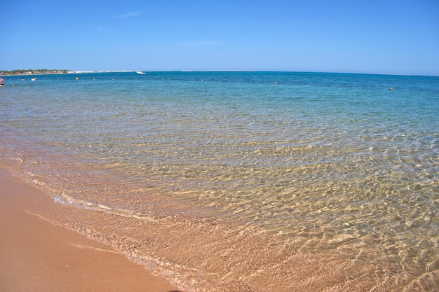 黄色い砂浜に小さな波紋の波が打ち寄せる青い海の水面の海景旅行と休暇のコンセプト