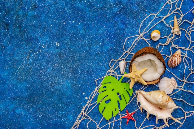 Seashells, net, coconut, starfishes and monstera leaf on blue glitter
