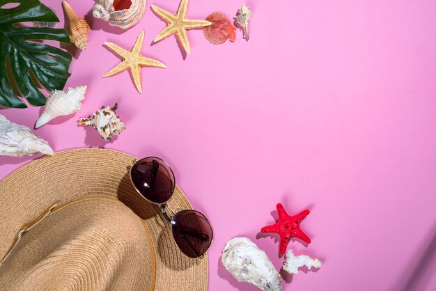 Seashells on pastel violet background with straw hat - summer holiday background