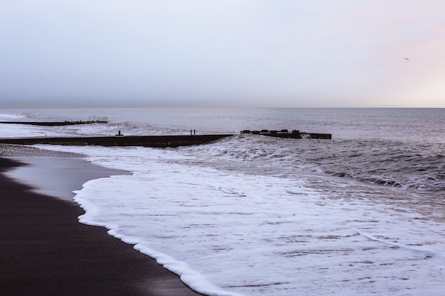 검은 모래, 하얀 거품과 스카이 라인이있는 해변