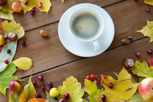 季節、飲み物、朝のコンセプト - 秋の紅葉と木製のテーブルの上のコーヒー カップのクローズ アップ