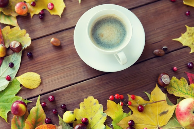 season, drink and morning concept - close up of coffee cup on wooden table with autumn leaves