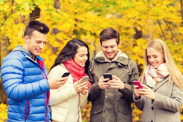 Season, people, technology and friendship concept - group of smiling friends with smartphones in autumn park