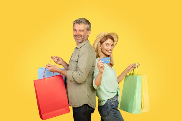 Фото Концепция сезонных продаж веселые европейские супруги среднего возраста, несущие красочные сумки и