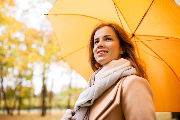 season, weather and people concept - beautiful happy young woman with yellow umbrella walking in autumn park