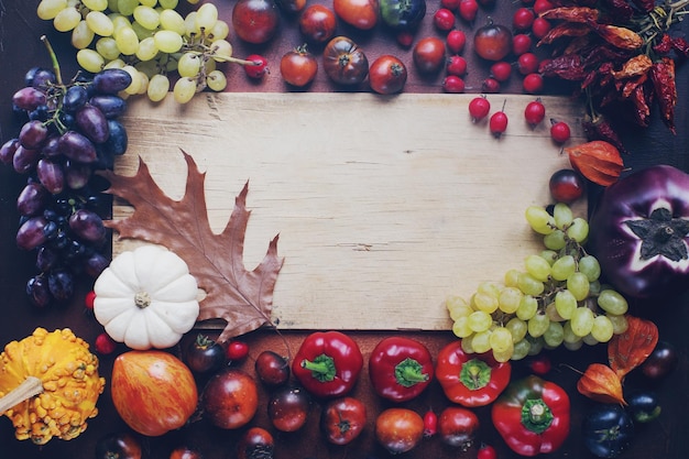 Seasonal composition with pumpkins grapes autumn leaves ripe fruits and vegetables on rustic wooden board with space for text halloween or thanksgiving background