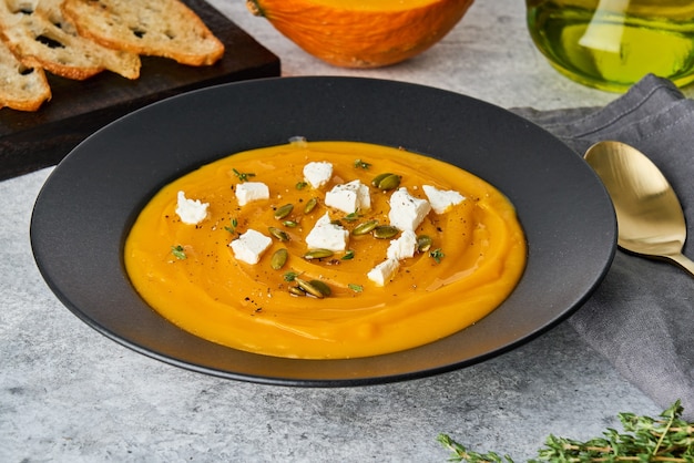 Seasonal pumpkin cream puree soup with feta cheese seeds thyme toast and olive oil