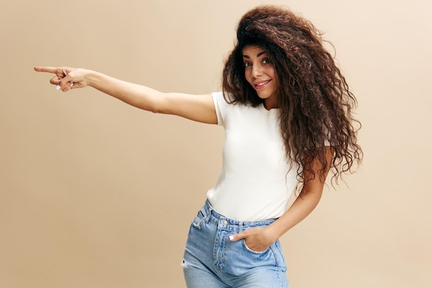 Seasonal sale offer excited beautiful latin female in white\
tshirt with afro say look at this look at camera show copy space\
free place for design ad fashion studio shoot over beige\
background