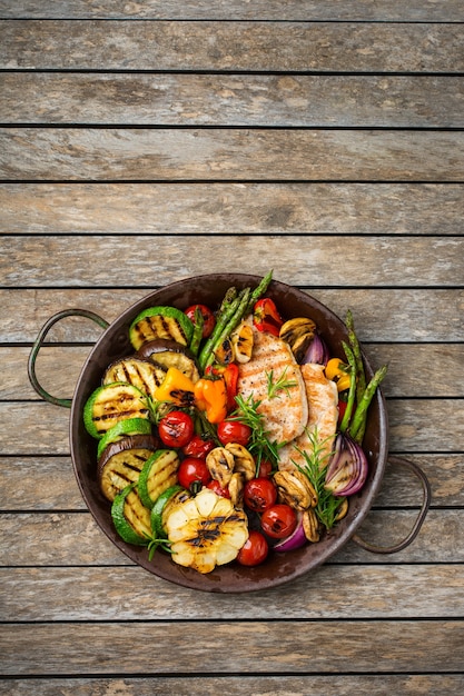 Seasonal, summer eating concept. Grilled vegetables and chicken breast in a pan on a wooden table. Top view flat lay copy space background