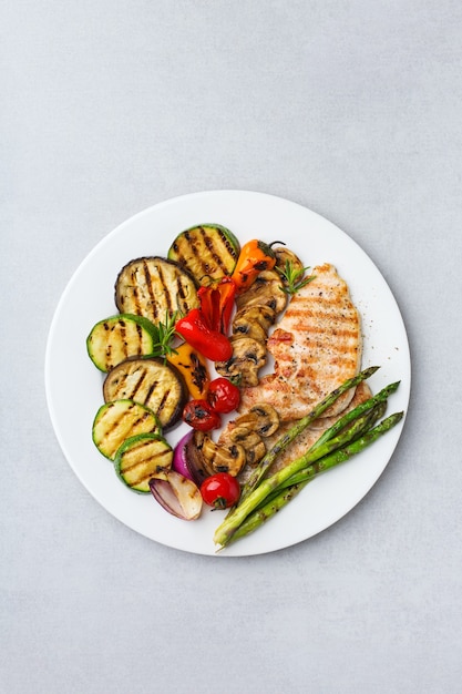 季節の夏の食事のコンセプト。白いテーブルの上の皿に野菜と鶏の胸肉のグリル。上面図フラットレイコピースペースの背景