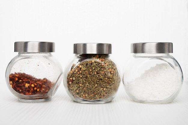 Seasoning in jars on a white background. Sea salt, mix of herbs, hot chili pepper