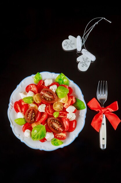 Seasoning sliced tomato with mozzarella salad, basil in plate on black. Top view.