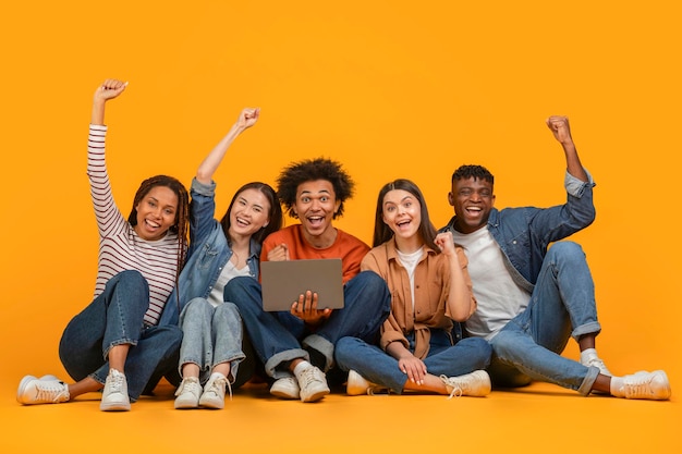 seated friends celebrating with a laptop on orange background