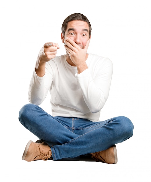 Seated young man laughing and pointing you