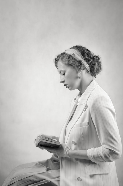 Seated young woman, dressed in retro style, reading a book. Studio portrait in profile