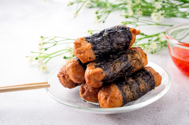 Seaweed Chicken Roll are stacked on a glass plate with chopsticks and sweet chilli sauces.