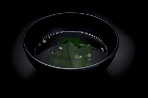 Photo seaweed soup (clear soup) on a black bowl on a black background.