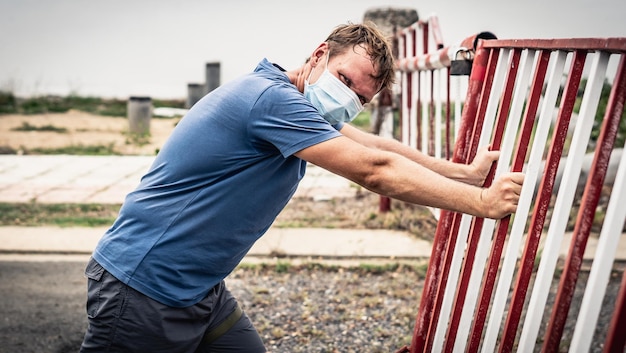 Second wave COVID Side view man look camera stand facing Red white iron fence door closed lock as sign of life crisis problem wants to overcome reach obstacle motivation work pressure Real people