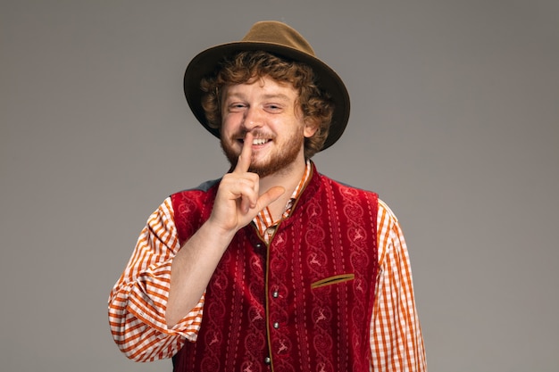 Segreto. sorridenti uomo vestito nel tradizionale costume austriaco o bavarese gesticolando isolato su grigio di sfondo per studio. copyspace. la celebrazione, l'oktoberfest, il festival, il concetto di tradizioni.