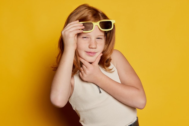 Secret and intrigue beautiful little girl with red hair and freckles wearing sunglasses isolated