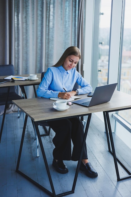 The secretary checks the schedule Cheerful young beautiful woman in glasses with a smile uses a laptop while sitting at her workplace