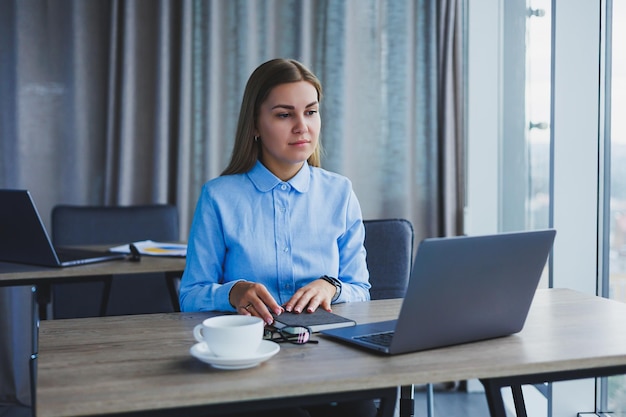 The secretary checks the schedule Cheerful young beautiful woman in glasses with a smile uses a laptop while sitting at her workplace