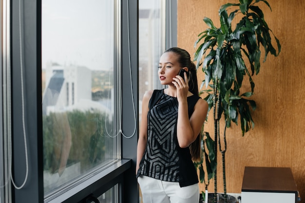 The secretary is talking on the phone near the window in the office