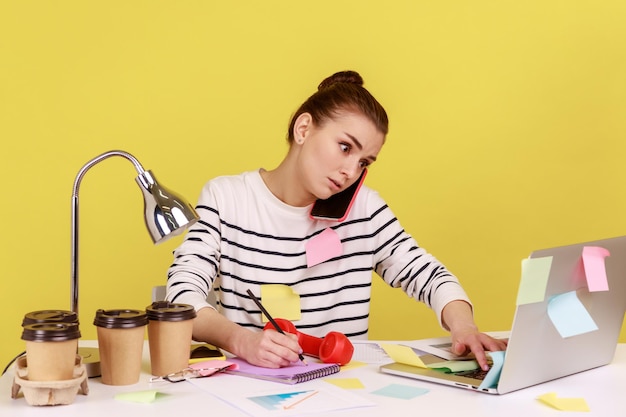 Secretary receiving calls on phone and making notes writing down information sitting at workplace