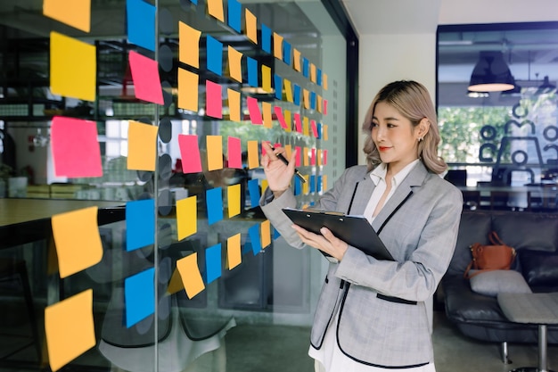 Secretary working in modern office in skyscraper writing and sticking adhesive notes with tasks on window modern officexA
