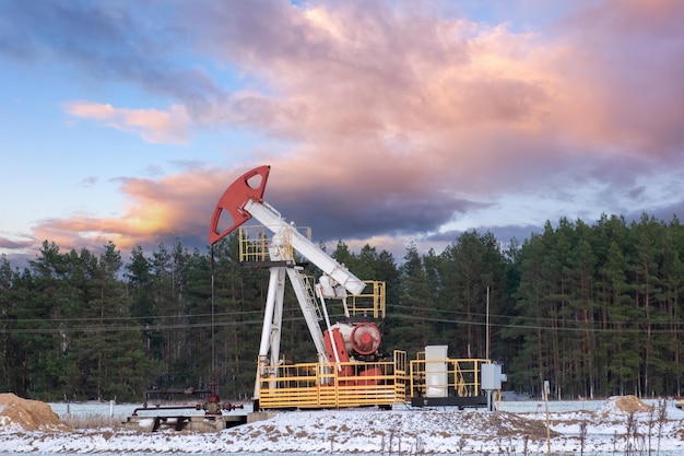 A section of an oil field where oil pumps operate winter Silhouette of a block pumping unit against a dramatic winter sky