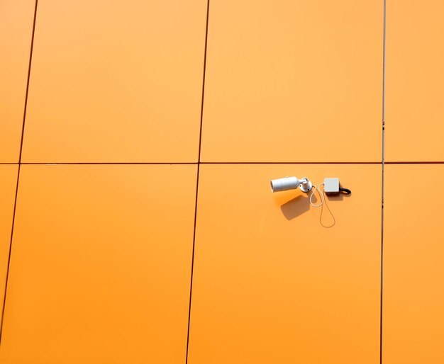 オレンジ色のパネルで仕上げられた現代の建物の壁に取り付けられた防犯カメラの接写