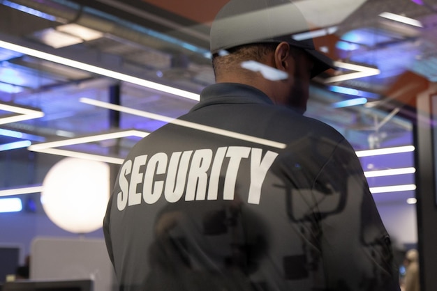 Foto guardia di sicurezza in piedi all'interno di un edificio commerciale vicino alla finestra che riflette la luce