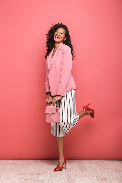 seductive american woman with curly hair laughing at camera isolated over pink wall